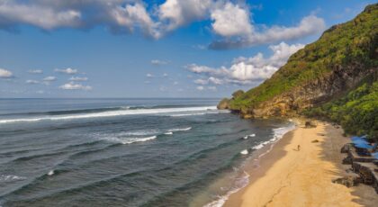 Explore the serene beauty of a Bali beach with azure waters, golden sands, and lush cliffs under a bright sky.