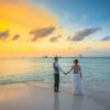 A romantic couple holding hands at sunset on a Maldives beach, exuding love and tranquility.